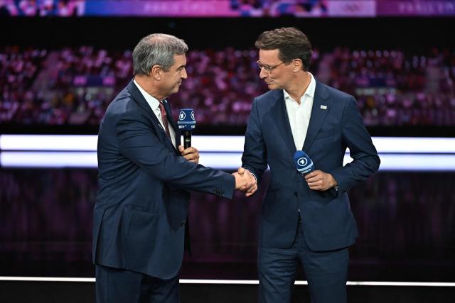 Bavaria's State Premier Markus Soeder (L) and North Rhine-Westphalia's State Premier Hendrik Wuest shake hands on stage at the Kurhaus in Baden-Baden, southwestern Germany, on September 26, 2026, during the German Olympic Sports Confederation's (DOSB) announcement of its national bid to host the Olympic Games in Germany. (Photo by Uwe ANSPACH / AFP)