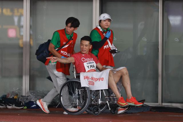 China's Ma Yinglong is being carried on wheelchair after an injury in the men's triple jump final during the 2026 Asian Games at Nagoya City Mizuho Park Athletic Stadium in Nagoya, Aichi Prefecture on September 26, 2026. (Photo by DAVID GRAY / AFP)