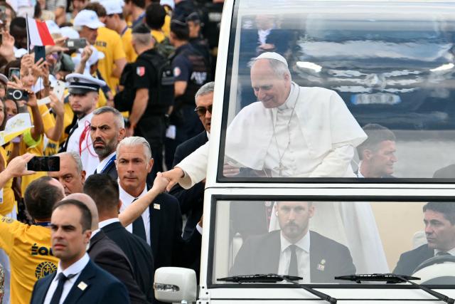 Pope Leo XIV shakes hands with a worshipper as he rides down the Champs-Elysees Avenue in his Papamobile (popemobile) on his way to celebrate a solemn outdoor mass at Place de la Concorde, central Paris, on September 26, 2026 on the second day of his visit to France. Pope Leo XIV celebrates an open-air mass for hundreds of thousands of believers on the Champs Elysees in Paris, after saying it was possible to "live together in dignity and peace". (Photo by Alberto PIZZOLI / AFP)