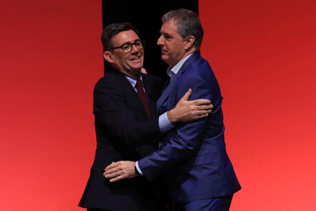 Britain's Prime Minister Andy Burnham (L) greets Liverpool mayor Steve Rotheram (R) on stage on the first day of the annual Labour Party conference in Liverpool, north-west England, on September 27, 2026. Britain's ruling Labour Party gathers Sunday for its first annual conference under Andy Burnham's leadership, heartened by his start as prime minister but now looking for concrete plans to tackle looming challenges. (Photo by Darren Staples / AFP)