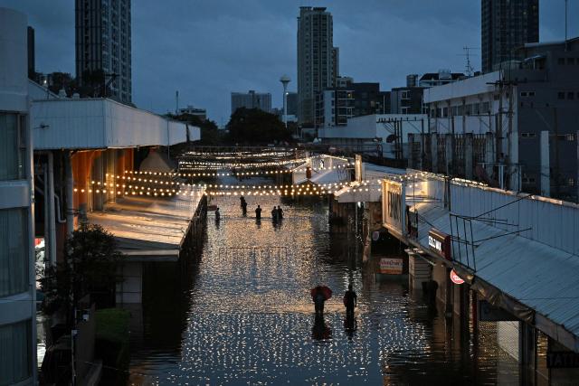 Residents wade through floodwaters in Bang Kapi district, Bangkok on September 27, 2026. Deep floodwaters in Bangkok drove thousands of residents into shelters as others scrambled to buy groceries or dry out their homes on September 27, after days of heavy rain inundated markets, roads and residences. (Photo by Lillian SUWANRUMPHA / AFP)