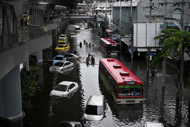 Residents navigate past abandoned vehicles as they wade through floodwaters at Bang Kapi district in Bangkok on September 27, 2026. Deep floodwaters in Bangkok drove thousands of residents into shelters as others scrambled to buy groceries or dry out their homes on September 27, after days of heavy rain inundated markets, roads and residences. (Photo by Lillian SUWANRUMPHA / AFP)