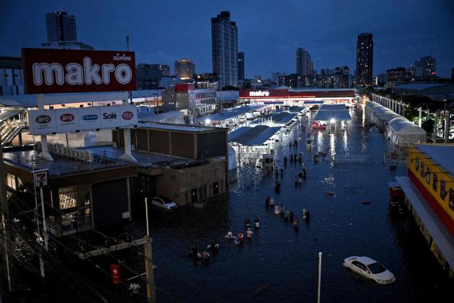 Residents wade through floodwaters after shopping at the Makro supermarket in Bang Kapi district, Bangkok on September 27, 2026. Deep floodwaters in Bangkok drove thousands of residents into shelters as others scrambled to buy groceries or dry out their homes on September 27, after days of heavy rain inundated markets, roads and residences. (Photo by Lillian SUWANRUMPHA / AFP)
