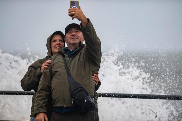 A couple takes a selfie as waves crash onto the shore during a noreaster storm in Hampton, New Hampshire, on September 27, 2026. A powerful autumnal storm lashed the heavily populated US Northeast corridor with wind, rain and large waves, knocking out power for thousands and killing at least one person. Nor'easters, as storms like these are known, can cause billions of dollars in damage as they bring torrential rain, sometimes snow, strong winds and heavy storm surge flooding to large swaths of the US East Coast. The National Weather Service (NWS) said Sunday morning that the storm was "slowly weakening" after causing days of havoc up and down the East Coast. (Photo by Joseph Prezioso / AFP)