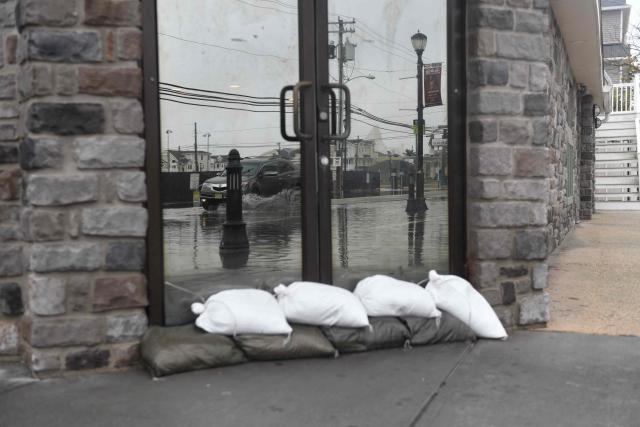 A truck is reflected in the door of a business protected by sandbags as it drives through a flooded street in Sea Isle City, New Jersey, on September 27, 2026. A powerful autumnal storm lashed the heavily populated US Northeast corridor with wind, rain and large waves, knocking out power for thousands and killing at least one person. Nor'easters, as storms like these are known, can cause billions of dollars in damage as they bring torrential rain, sometimes snow, strong winds and heavy storm surge flooding to large swaths of the US East Coast. The National Weather Service (NWS) said Sunday morning that the storm was "slowly weakening" after causing days of havoc up and down the East Coast. (Photo by Matthew HATCHER / AFP)