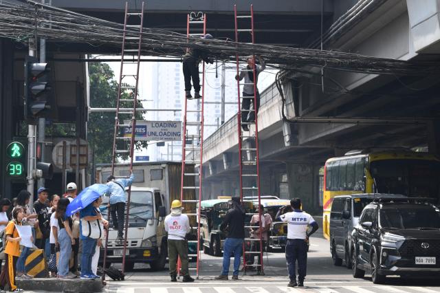 Workers standing on ladders fix cable wires along a road in Manila on September 28, 2026. The Department of Labour and Employment issued a new wage order, effective September 26, of 60 peso (96 cents USD) wage increase in the metropolis, as the country struggles to deal with soaring fuel costs from the Middle East war. (Photo by Ted ALJIBE / AFP)