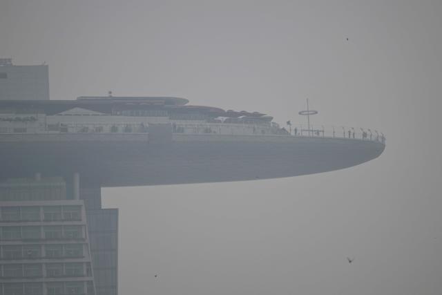 People stand on the observation deck of the Marina Bay Sands on a hazy day in Singapore September 28, 2026. Indonesia has been battling fires for weeks in parts of Borneo and Sumatra, sending suffocating haze across the islands and neighbouring Malaysia and Singapore. (Photo by Roslan RAHMAN / AFP)