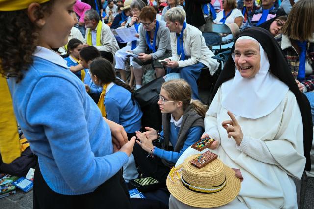 A nun plays mastermind with a girl scout as they wait outside the Saint-Etienne Cathedral in Metz, northeastern France, where the Pope will celebrate a mass later on September 28, 2026 on the last day of the Pope visit to France. (Photo by SEBASTIEN BOZON / AFP)