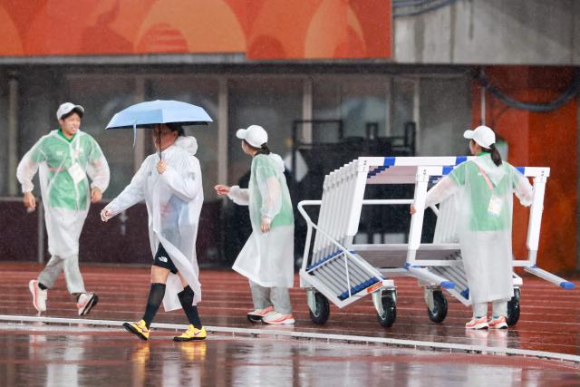 An official wearing a poncho pushes a trolly with hurdles on ahead of the track and field session during the 2026 Asian Games at Nagoya City Mizuho Park Athletic Stadium in Nagoya, Aichi Prefecture on September 28, 2026. (Photo by DAVID GRAY / AFP)