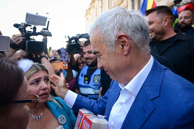 Romania's far-right politician and former presidential candidate Calin Georgescu pats one of his supporters as he leaves the Court of Appeal in Bucharest on September 28, 2026, following a new hearing in the case in which he and other defendants are accused of actions against Romanias constitutional order. The hearing marks the continuation of proceedings after the court postponed the first trial session earlier in September 2026. Hundreds of Georgescu's supporters gathered outside the courthouse in support of him. Georgescu in 2024 unexpectedly won the first round of a presidential election but it was cancelled over allegations of Russian interference. (Photo by Daniel MIHAILESCU / AFP)