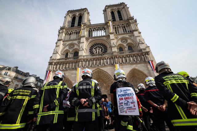 Firefighters observe a minute of silence in memory of their comrades killed while battling wildfires in France, in front of Notre-Dame de Paris Cathedral during a protest called by a broad coalition of unions campaigning for higher pay and increased budgetary resources, in Paris, on September 28, 2026. Professional firefighters, who are local government employees, together with around 200,000 volunteer firefighters, are calling for increased recruitment, stronger health protections, and a clearer focus on their core duties. (Photo by Xavier GALIANA / AFP)
