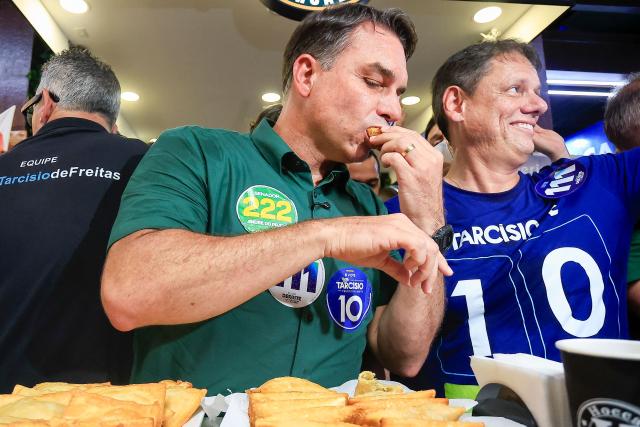 Brazil's right-wing senator and presidential candidate Flavio Bolsonaro (C), of the Liberal Party (PL), next to Sao Paulo's governor Tarcisio de Freitas tries a traditional fried pastry during a campaign rally at the Sao Paulo Municipal Market in Sao Paulo, Brazil, on September 28, 2026. Brazil will hold presidential election on October 4, 2026. (Photo by Miguel SCHINCARIOL / AFP)