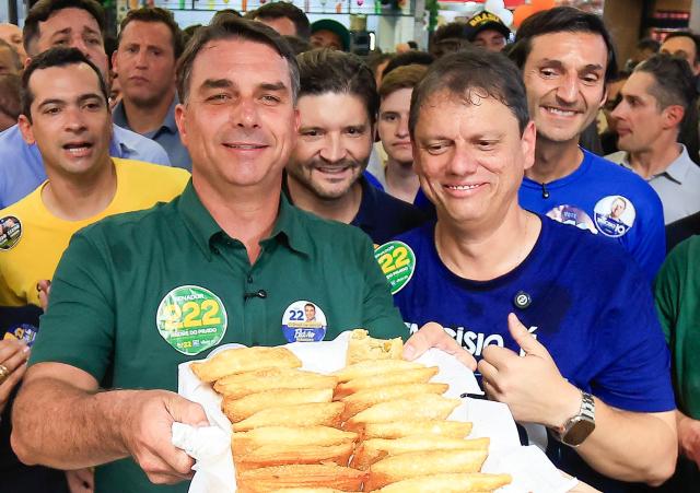 Brazil's right-wing senator and presidential candidate Flavio Bolsonaro (L), of the Liberal Party (PL), next to Sao Paulo's governor Tarcisio de Freitas holds a tray with traditional fried pastry during a campaign rally at the Sao Paulo Municipal Market in Sao Paulo, Brazil, on September 28, 2026. Brazil will hold presidential election on October 4, 2026. (Photo by Miguel SCHINCARIOL / AFP)