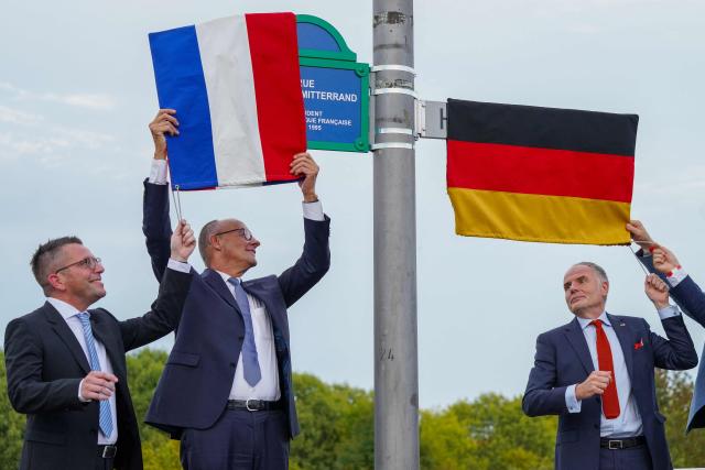 German Chancellor Friedrich Merz (C), Marc Speicher (L), Mayor of Saarlouis, and Jerome Spinoza (R), Consul General of France in Saarland, unveil the streets in honor of the late former German chancellor Helmut Kohl and the late former French president Francois Mitterrand, in Saarlouis, western Germany on September 28 2026. German Chancellor Friedrich Merz (C), Marc Speicher (L), Mayor of Saarlouis, (Photo by Andreas Schlichter / AFP)