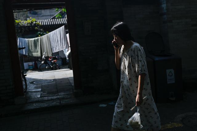 A woman carrying a bag of food uses her mobile phone while walking past a courtyard house along an alley in Beijing on September 29, 2026. (Photo by WANG Zhao / AFP)