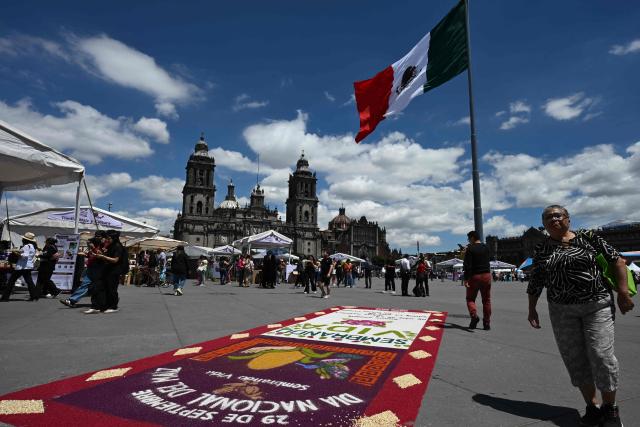 Attendees walk past a carpet made of corn kernels of various colours during the National Corn Day commemoration in Mexico City's Zocalo Square on September 29, 2026. The Mexican government, together with farmers, peasant organisations and civil society groups, is showcasing products derived from Mexico's 64 native maize varieties, considered a symbol of national identity and cultural heritage. (Photo by Yuri CORTEZ / AFP)