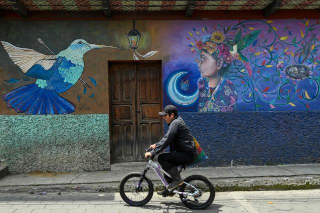 A cyclist rides past a mural depicting a hummingbird and an indigenous girl  on the streets of Santa Maria de Jesus, Guatemala,on September 30, 2026. The murals are part of “"A New Air for Santa Maria de Jesus" an initiative that seeks to restore deteriorated spaces and strengthen the identity of this community through art. (Photo by Johan ORDONEZ / AFP)