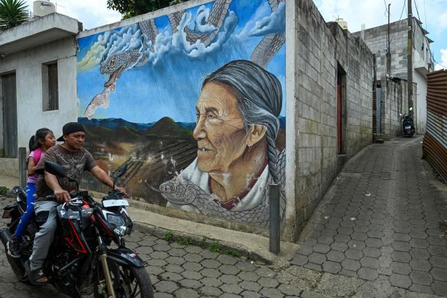 A rider past a mural of the indigenus woman on the streets of Santa Maria de Jesus, Guatemala,on September 30, 2026. The murals are part of “"A New Air for Santa Maria de Jesus" an initiative that seeks to restore deteriorated spaces and strengthen the identity of this community through art. (Photo by Johan ORDONEZ / AFP)