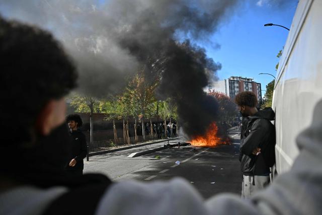 Protesting students look at a burnt barrier during a blockading action outside the secondary school Le Corbusier, in Aubervilliers, northern Paris on October 1, 2026. Since late September, students have staged protests outside schools over grievances ranging from timetables, class sizes and a shortage of teachers to overheated classrooms during this year's heatwaves. The protests started in the Ile-de-France region around Paris but have now spread to other cities nationwide. (Photo by LOU BENOIST / AFP)