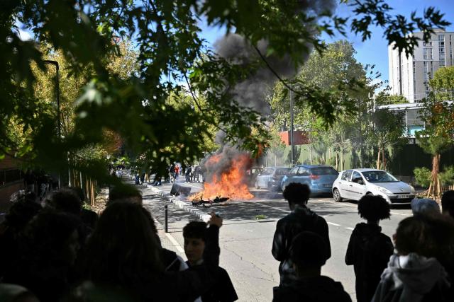 Protesting students look at a burnt barrier during a blockading action outside the secondary school Le Corbusier, in Aubervilliers, northern Paris on October 1, 2026. Since late September, students have staged protests outside schools over grievances ranging from timetables, class sizes and a shortage of teachers to overheated classrooms during this year's heatwaves. The protests started in the Ile-de-France region around Paris but have now spread to other cities nationwide. (Photo by LOU BENOIST / AFP)