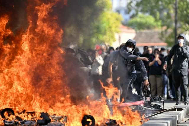 A protesting student feeds a burnt barrier during a blockading action outside the secondary school Le Corbusier, in Aubervilliers, northern Paris on October 1, 2026. Since late September, students have staged protests outside schools over grievances ranging from timetables, class sizes and a shortage of teachers to overheated classrooms during this year's heatwaves. The protests started in the Ile-de-France region around Paris but have now spread to other cities nationwide. (Photo by LOU BENOIST / AFP)
