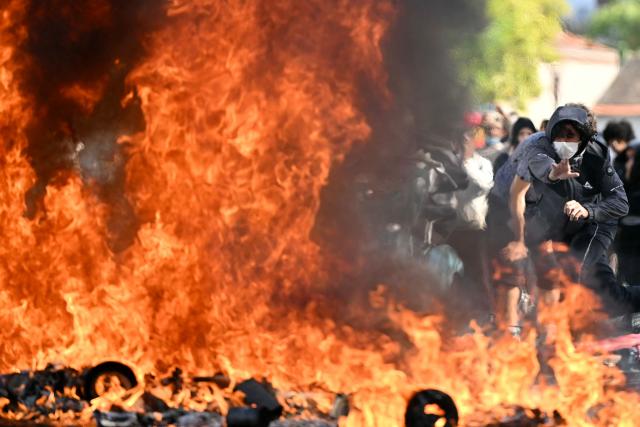 A protesting student feeds a burnt barrier during a blockading action outside the secondary school Le Corbusier, in Aubervilliers, northern Paris on October 1, 2026. Since late September, students have staged protests outside schools over grievances ranging from timetables, class sizes and a shortage of teachers to overheated classrooms during this year's heatwaves. The protests started in the Ile-de-France region around Paris but have now spread to other cities nationwide. (Photo by LOU BENOIST / AFP)