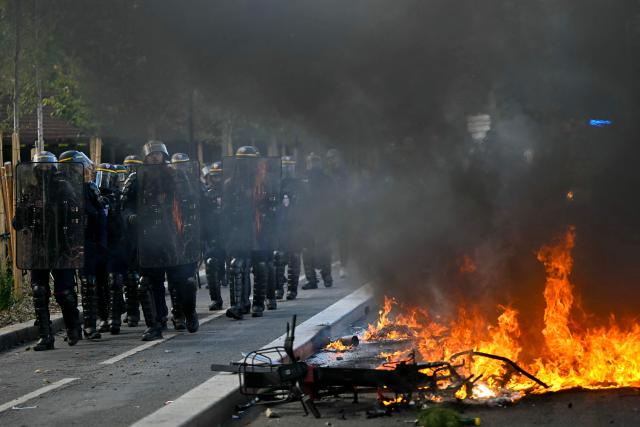 Anti-riot police officers stand walk past a burnt barrier while protesting students carry out blockading action in Aubervilliers, northern Paris on October 1, 2026. Since late September, students have staged protests outside schools over grievances ranging from timetables, class sizes and a shortage of teachers to overheated classrooms during this year's heatwaves. The protests started in the Ile-de-France region around Paris but have now spread to other cities nationwide. (Photo by LOU BENOIST / AFP)