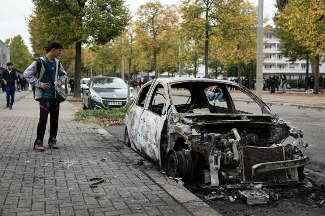 A student looks at a burnt car following a student blockading protest, in Strasbourg eastern France, on October 1, 2026. Since late September, students have staged protests outside schools over grievances ranging from timetables, class sizes and a shortage of teachers to overheated classrooms during this year's heatwaves. The protests started in the Ile-de-France region around Paris but have now spread to other cities nationwide. (Photo by ROMEO BOETZLE / AFP)