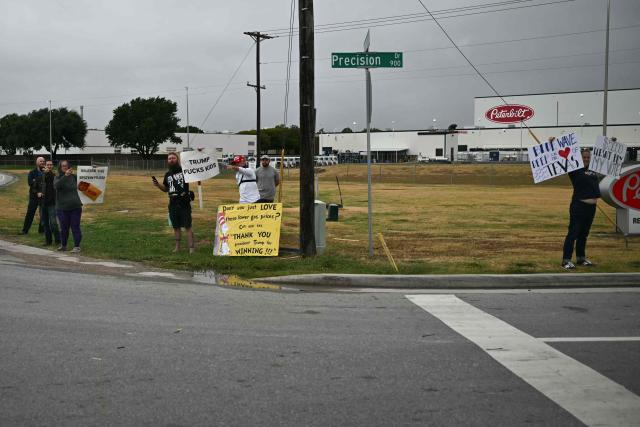 Protestors hold signs as the motorcade of US President Donald Trump drives by near Dallas Fort Worth International Airport in Dallas, Texas, on October 1, 2026. Trump is travelling to Texas and Oklahoma to speak at campaign rallies. (Photo by Kent NISHIMURA / AFP)