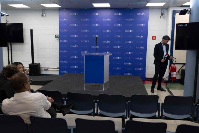 A journalist stands next to an empty lectern at TV Globo studios after the cancellation of the presidential debate in Rio de Janeiro, Brazil on October 1, 2026. The debate was cancelled after Brazil's President and Presidential candidate Luiz Inacio Lula da Silva and right-wing Presidential candidate Flavio Bolsonaro refused to attend. (Photo by Pablo PORCIUNCULA / AFP)
