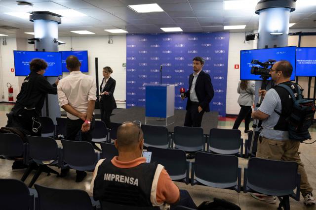 Journalists stand next to an empty lectern at TV Globo studios after the cancellation of the presidential debate in Rio de Janeiro, Brazil on October 1, 2026. The debate was cancelled after Brazil's President and Presidential candidate Luiz Inacio Lula da Silva and right-wing Presidential candidate Flavio Bolsonaro refused to attend. (Photo by Pablo PORCIUNCULA / AFP)