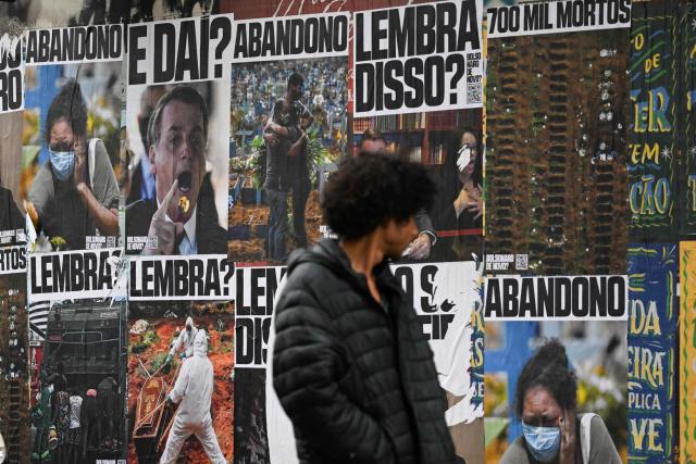 A man looks at posters refering to convicted former Brazilian President Jair Bolsonaro and the COVID-19 pandemic, in Sao Paulo, Brazil on October 2, 2026. Next October 4 Brazil's President and re-election candidate Luiz Inacio Lula da Silva faces off against the 45-year-old right-wing senator Flavio Bolsonaro, who is trying to ride the regional conservative wave encouraged by US President Donald Trump. (Photo by Luis ROBAYO / AFP)