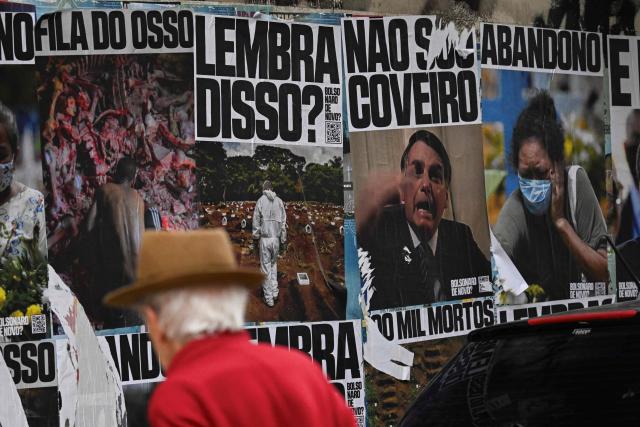 A man looks at posters refering to convicted former Brazilian President Jair Bolsonaro and the COVID-19 pandemic, in Sao Paulo, Brazil on October 2, 2026. Next October 4 Brazil's President and re-election candidate Luiz Inacio Lula da Silva faces off against the 45-year-old right-wing senator Flavio Bolsonaro, who is trying to ride the regional conservative wave encouraged by US President Donald Trump. (Photo by Luis ROBAYO / AFP)