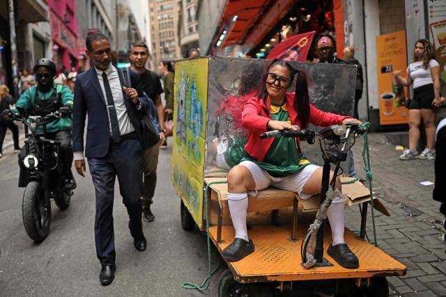 A passer by looks at a woman disguised as La Chilindrina -fictional character of Mexican television series El Chavo del Ocho- as she poses for a photo in downtown Sao Paulo, Brazil on October 2, 2026. Brazilians will go to the polls next October 4 once again deeply polarized and under the shadow of US President Donald Trump, who has backed conservative candidates in recent elections in Latin America. (Photo by Luis ROBAYO / AFP)