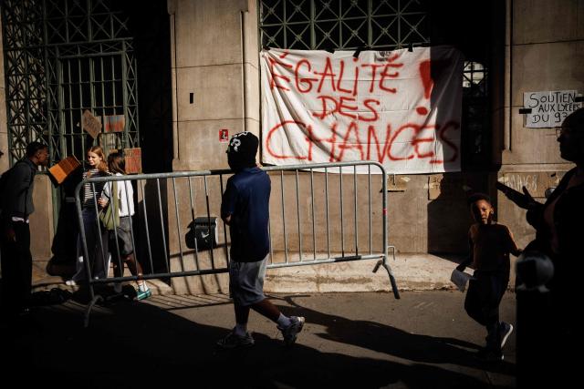 A student carries a barrier in front of a banner which reads "equal opportunities" suspended on the front of Louis-le-Grand high school in central Paris, on October 2, 2026. Since late September, students have staged protests outside schools over grievances ranging from timetables, class sizes and a shortage of teachers to overheated classrooms during this year's heatwaves. The protests started in the Ile-de-France region around Paris but have now spread to other cities nationwide. (Photo by Simon WOHLFAHRT / AFP)