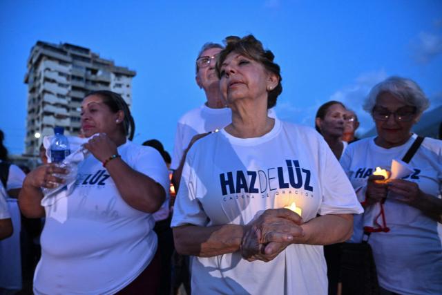 People hold candles during a vigil and prayer service called "Beam of Light," marking 100 days since the twin earthquakes that struck Venezuela on June 24, killing and displacing thousands of people, in Caraballeda, La Guaira state, Venezuela, on October 2, 2026. (Photo by Juan BARRETO / AFP)