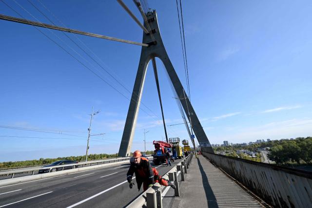 Technicians repair a trolleybus power line that was damaged following a drone attack on the Northern Bridge in Kyiv on October 3, 2026, amid Russian invasion of Ukraine. A Russian strike targeted a major bridge in Kyiv, its mayor said October 3, in another attack on Ukrainian infrastructure that has brought traffic chaos to the capital. The attack on the Northern Bridge, which followed a drone alert, came a day after the Southern Bridge was hit in a wave of strikes that city officials say is "tearing Kyiv apart". (Photo by Sergei SUPINSKY / AFP)