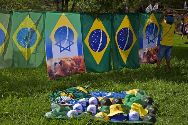 A man hangs flags for sale during Brazil's right-wing senator and presidential candidate Flavio Bolsonaro campaign rally on the eve of the general election, in Santa Barbara d'Oeste, state of Sao Paulo, Brazil on October 3, 2026. Brazilians go to the polls on October 4, 2026, in a tight race led by leftist President Luiz Inacio Lula da Silva and right-wing senator Flavio Bolsonaro, son of imprisoned former president Jair Bolsonaro. (Photo by NELSON ALMEIDA / AFP)