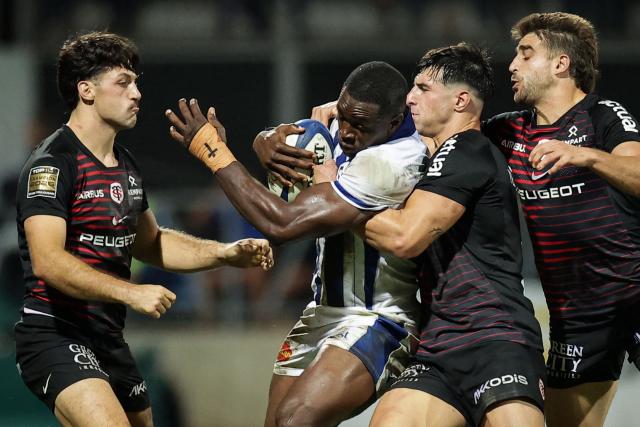 Castres' Cameroonian wing Christian Ambadiang (C) is tackled during the French Top14 rugby union match between Castres Olympique and Stade Toulousain at Stade Pierre Fabre in Castres, southwestern France, on October 3, 2026. (Photo by Valentine CHAPUIS / AFP)