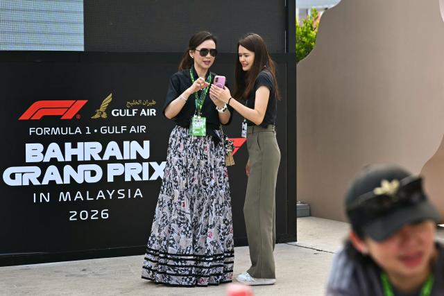 People use their mobile phones as they stand in front of signage for the Formula One Bahrain Grand Prix in Sepang on October 4, 2026. (Photo by Lillian SUWANRUMPHA / AFP)