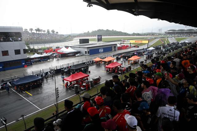 Teams gather around the cars as the start of the race has been delayed due to heave rain at the Formula One Bahrain Grand Prix in Sepang on October 4, 2026. (Photo by JADE GAO / AFP)