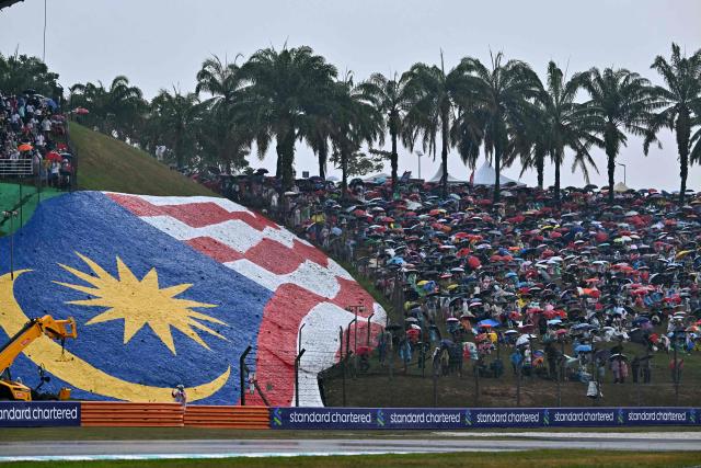 Spectators hold umbrellas as the rain delayed the start of the Formula One Bahrain Grand Prix in Sepang on October 4, 2026. (Photo by Lillian SUWANRUMPHA / AFP)