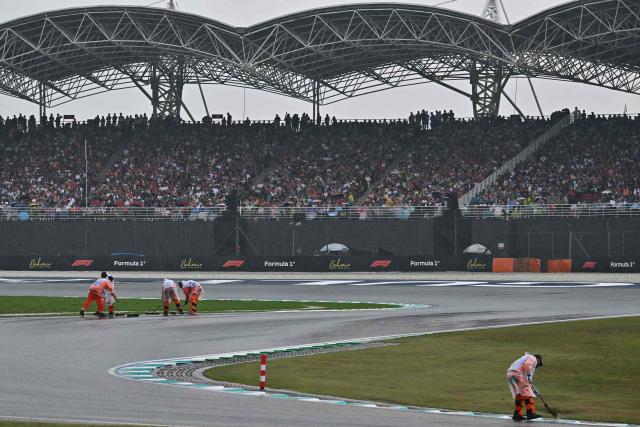 Track marshals sweep water off the track as rain delayed the start of the Formula One Bahrain Grand Prix in Sepang on October 4, 2026. (Photo by Lillian SUWANRUMPHA / AFP)