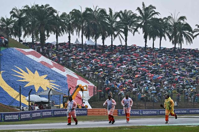 Spectators hold umbrellas as the rain delayed the start of the Formula One Bahrain Grand Prix in Sepang on October 4, 2026. (Photo by Lillian SUWANRUMPHA / AFP)