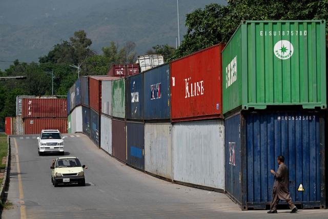 Commuters drive past shipping containers placed by authorities to block access to the Red Zone area in Islamabad on October 4, 2026, ahead of a protest by opposition party Pakistan Tehreek-e-Insaf (PTI) demanding the release of their leader and former prime minister Imran Khan. Talks between Pakistan's government and the party of jailed former prime minister Imran Khan aimed at avoiding a major demonstration stalled on October 4, with supporters vowing to go ahead with their protest. (Photo by Aamir QURESHI / AFP)