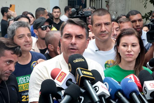 Brazil's right-wing senator and presidential candidate for the Liberal Party (PL) Flavio Bolsonaro (L) speaks to the media beside his wife Fernanda Bolsonaro as he leaves a polling station after voting during the presidential election in Rio de Janeiro, Brazil, on October 4, 2026. Brazilians head to the polls deeply polarized in a nail-biting first-round presidential election and under the shadow of US President Donald Trump, who has backed conservative candidates in recent elections in Latin America. (Photo by Douglas SHINEIDR / AFP)
