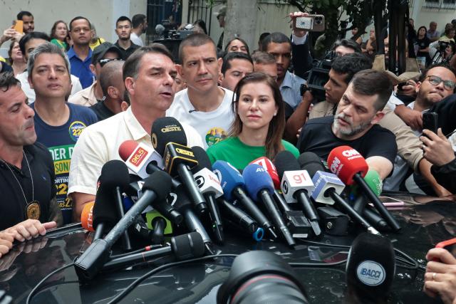 Brazil's right-wing senator and presidential candidate for the Liberal Party (PL) Flavio Bolsonaro (L) speaks to the media beside his wife Fernanda Bolsonaro as he leaves a polling station after voting during the presidential election in Rio de Janeiro, Brazil, on October 4, 2026. Brazilians head to the polls deeply polarized in a nail-biting first-round presidential election and under the shadow of US President Donald Trump, who has backed conservative candidates in recent elections in Latin America. (Photo by Douglas SHINEIDR / AFP)
