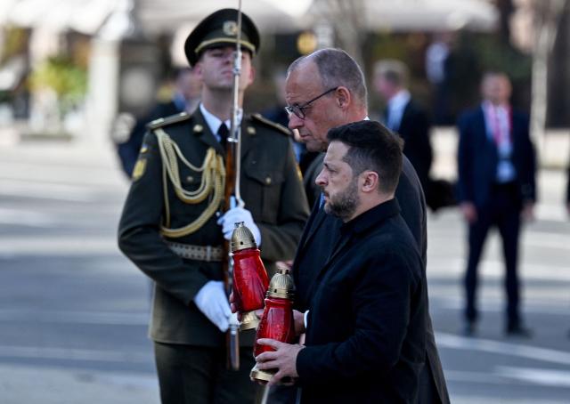 Ukraine's President Volodymyr Zelensky (bottom R) and Germany's Chancellor Friedrich set candles at a makeshift memorial for Ukrainian and foreign soldiers on Independence Square in Kyiv on October 4, 2026, amid the Russian invasion of Ukraine. (Photo by Sergei SUPINSKY / AFP)