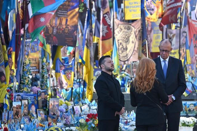Ukraine's President Volodymyr Zelensky (L) and Germany's Chancellor Friedrich Merz (R) stand next to a makeshift memorial for Ukrainian and foreign soldiers on Independence Square in Kyiv on October 4, 2026, amid the Russian invasion of Ukraine. (Photo by Sergei SUPINSKY / AFP)