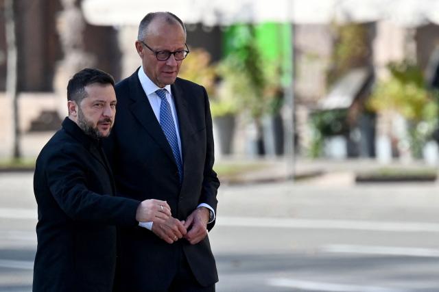 Ukraine's President Volodymyr Zelensky (L) and Germany's Chancellor Friedrich Merz meet prior to a ceremony near a makeshift memorial for Ukrainian and foreign soldiers on Independence Square in Kyiv on October 4, 2026, amid the Russian invasion of Ukraine. (Photo by Sergei SUPINSKY / AFP)